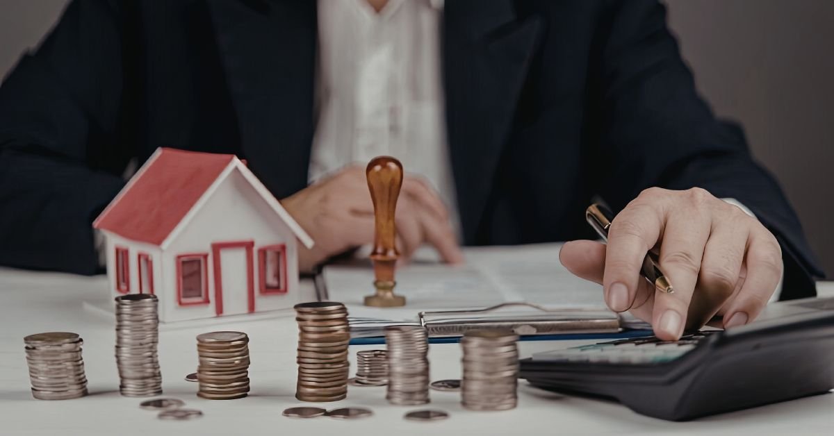 Person calculating property finances at desk with house model, stacked coins, calculator, and documents, representing real estate investment, budgeting, mortgage planning, and financial analysis.
